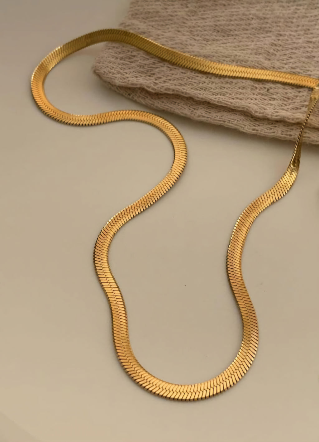 Gold snake-shaped necklace on a beige surface