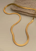 Gold snake-shaped necklace on a beige surface