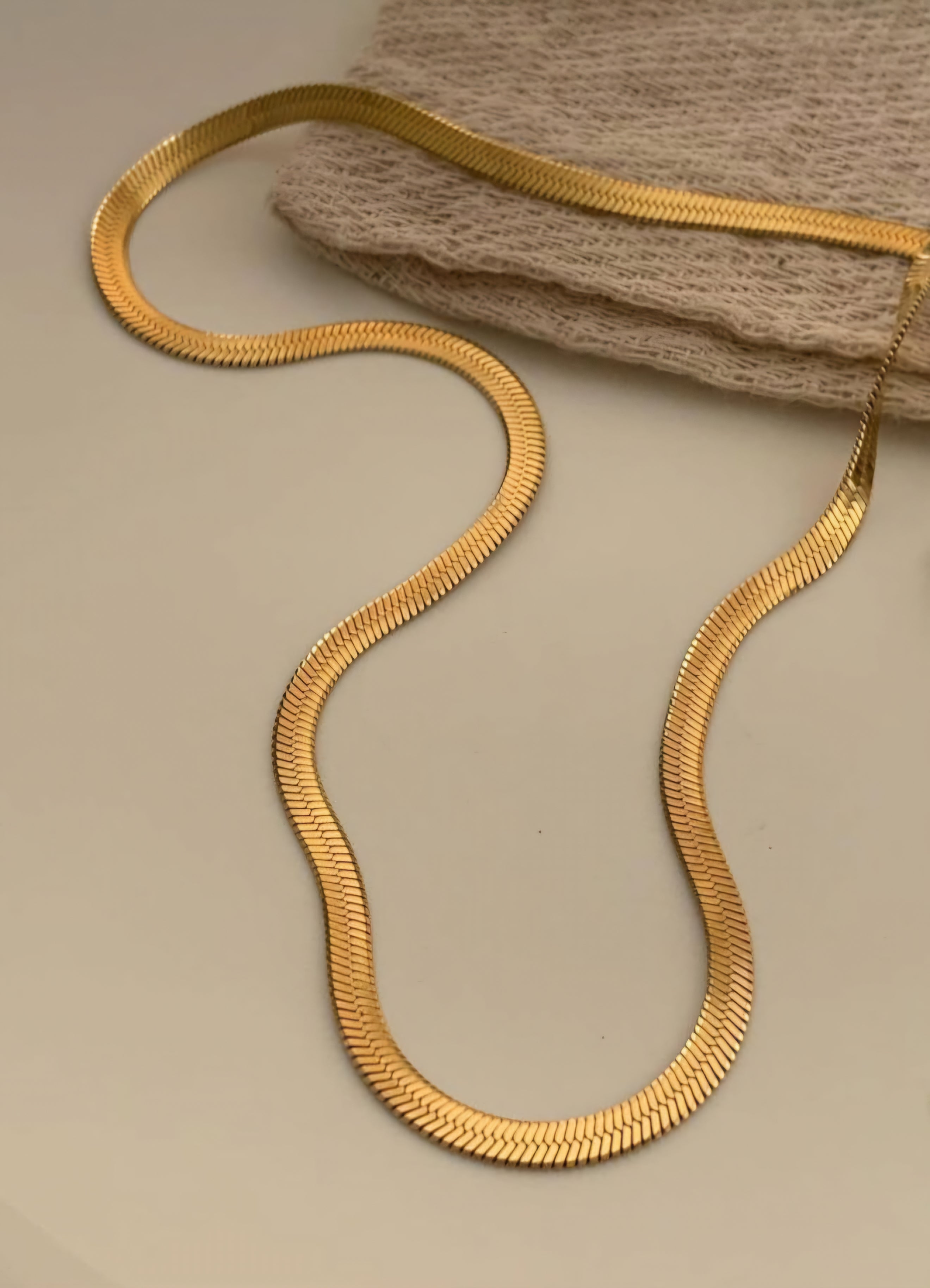 Gold snake-shaped necklace on a beige surface