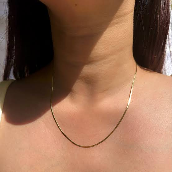 Golden anti tarnish snake chain on a person's neck with a neutral background