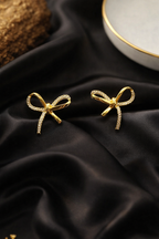 Gold bow-shaped earrings on black satin fabric