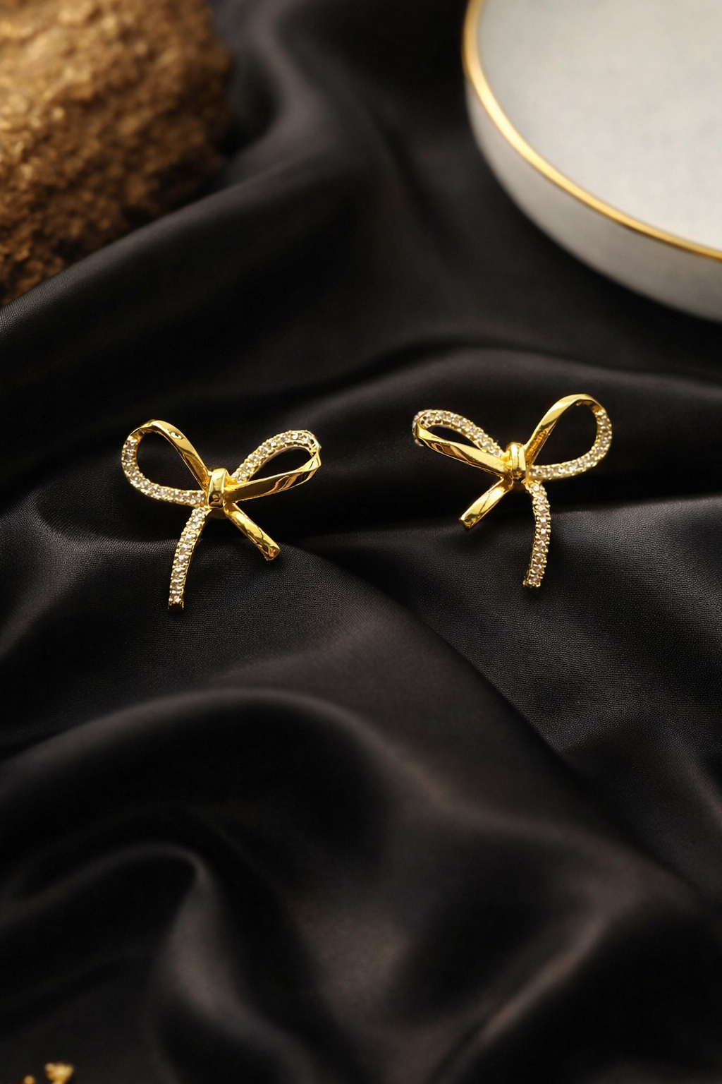Gold bow-shaped earrings on black satin fabric