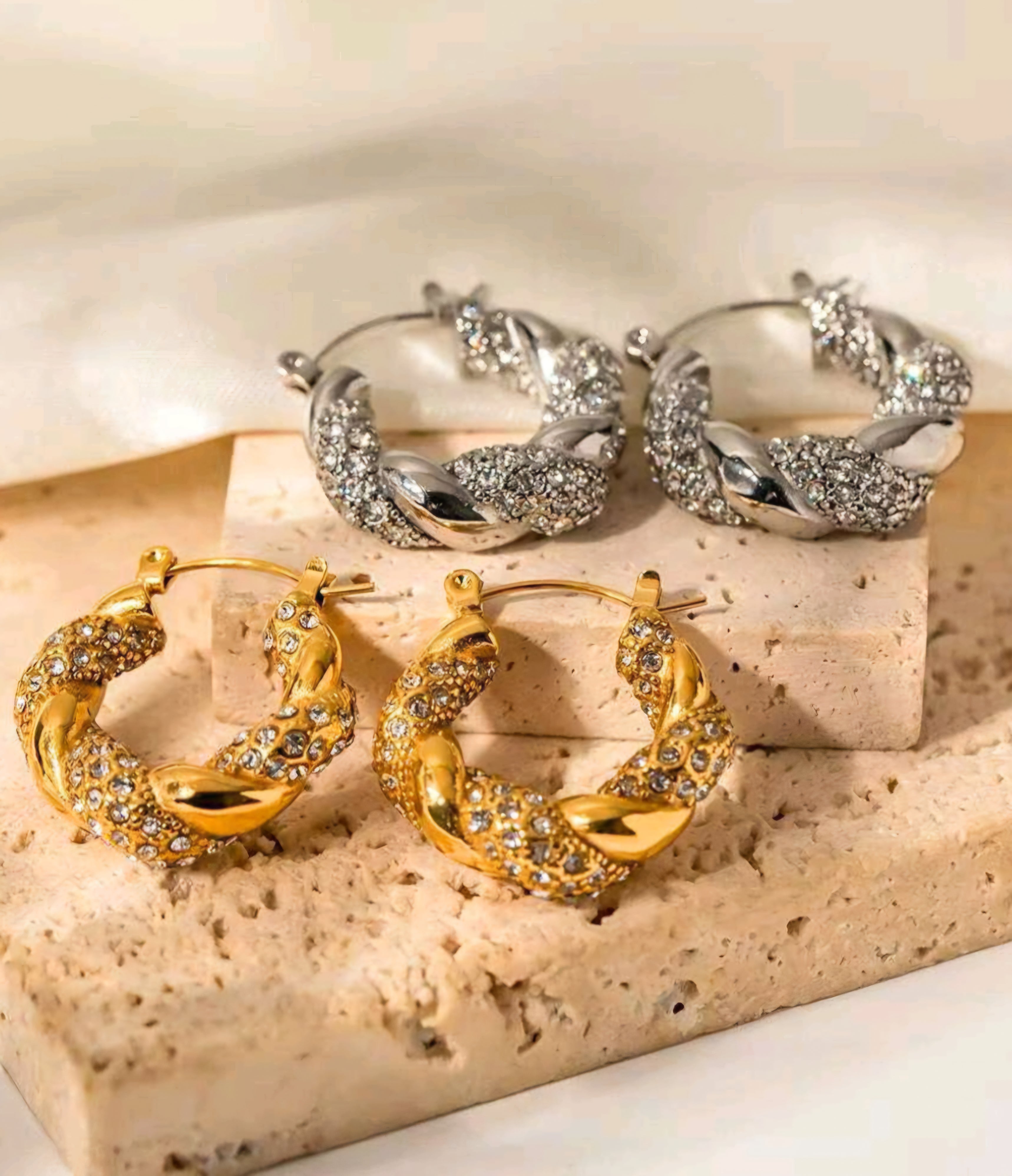 Pair of gold hoop earrings on a beige stone surface.