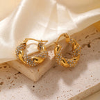 Gold hoop earrings with gemstones on a beige fabric background