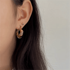 Close-up of an ear wearing a gold hoop earring with small stones on a neutral background