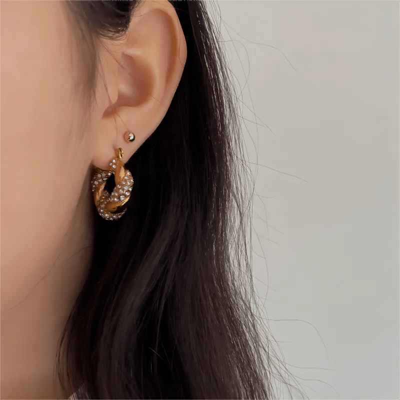 Close-up of an ear wearing a gold hoop earring with small stones on a neutral background