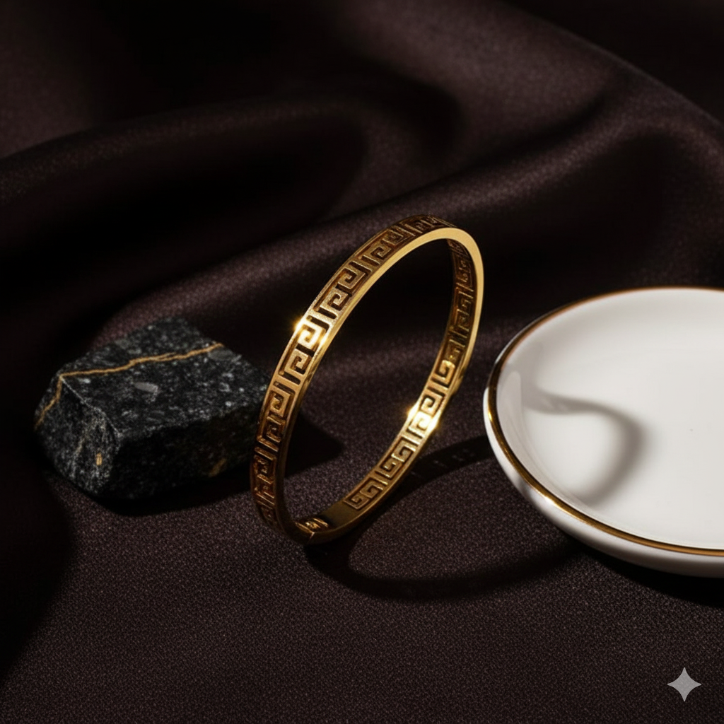 Versace Inspired Bangle - Gold Valerio bracelet on a dark fabric background with a white dish and stone.