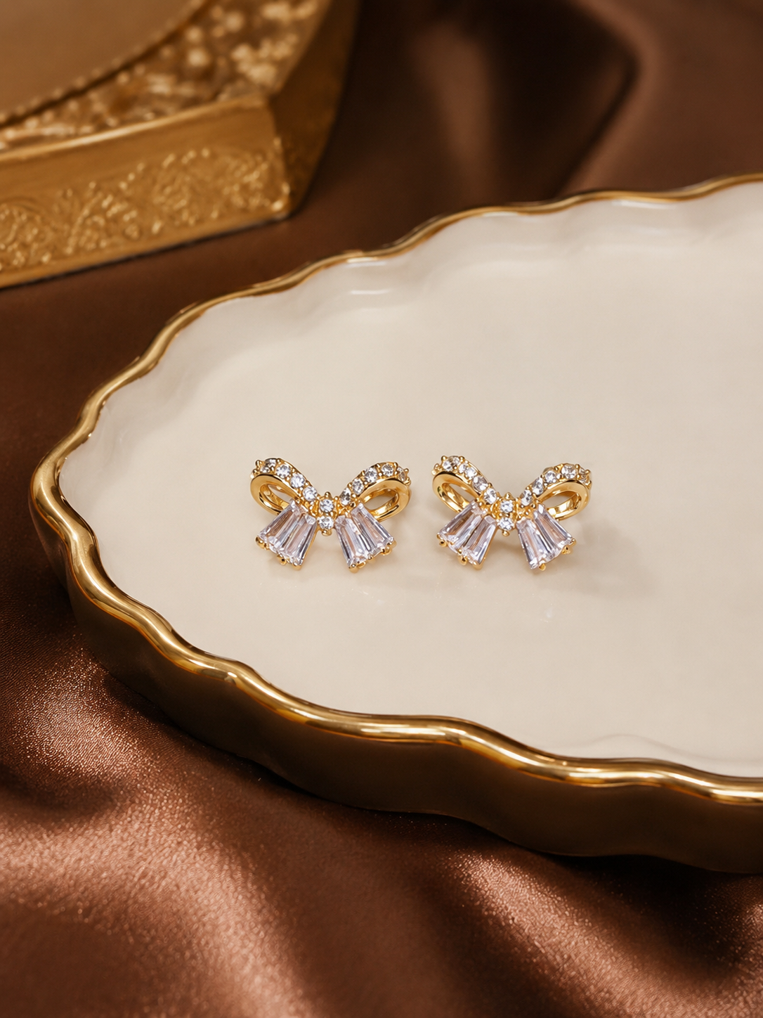 Anti tarnish bow-shaped earrings with clear stones on a decorative plate with a brown fabric background