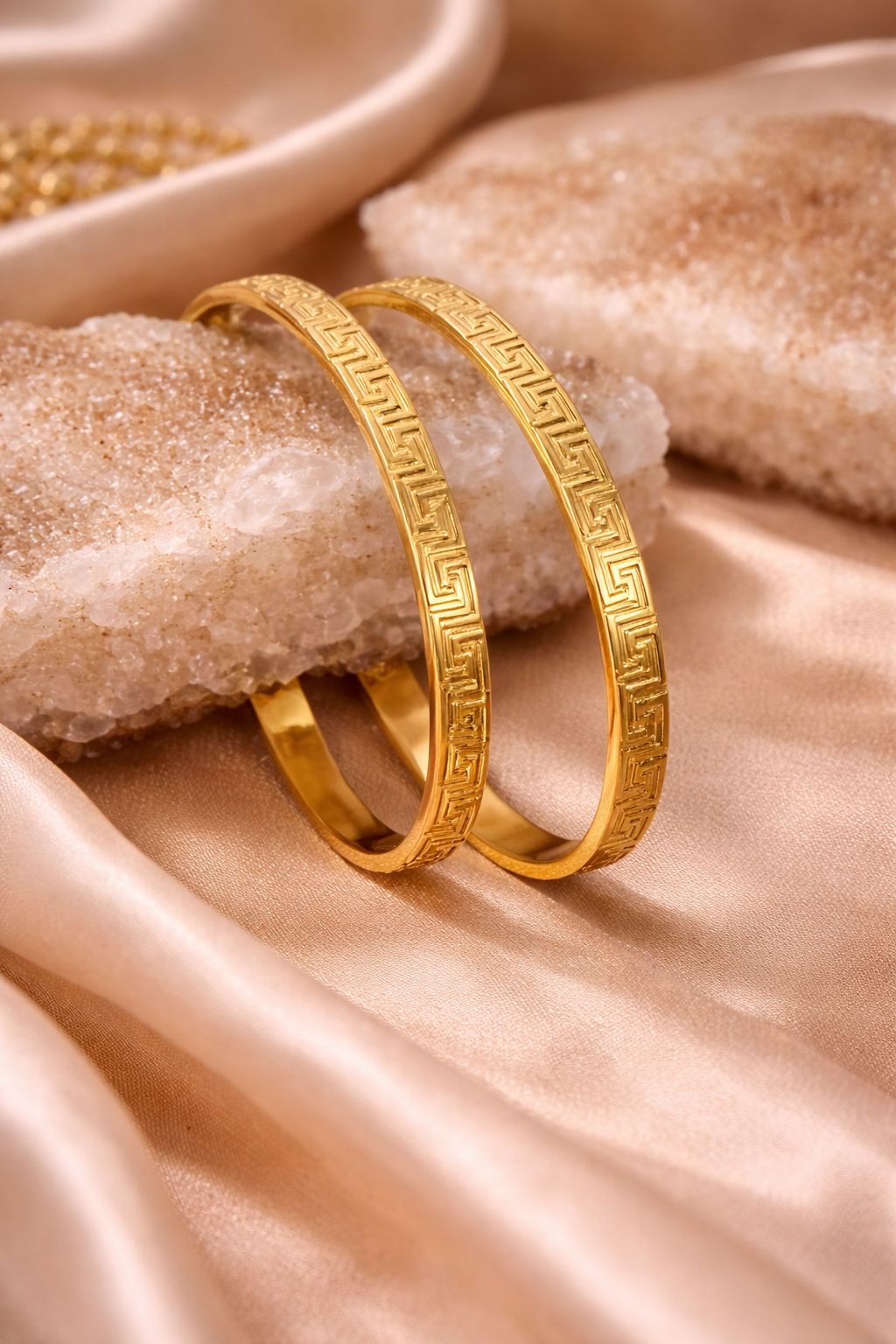 Two gold bracelets on a textured beige surface