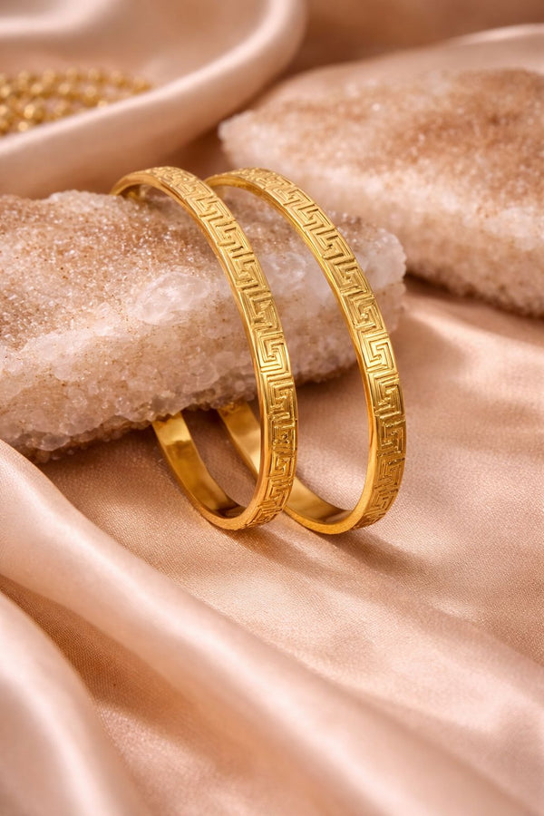 Two gold bracelets on a textured beige surface