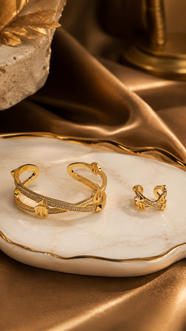 Gold bracelet and ring on a marble surface with a gold leaf and fabric background